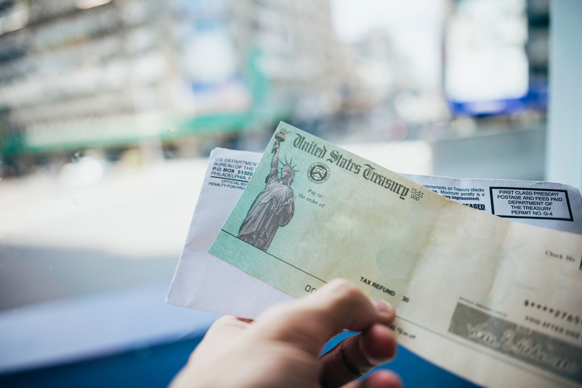 A woman is holding a tax refund check in her hand in the living room of her home.